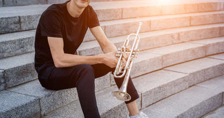 Young street musician playing guitar sitting on granite stepsの写真素材