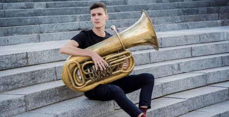 Young street musician playing tuba sitting on granite stepsの写真素材