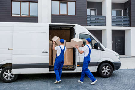 Two removal company workers unloading boxes from minibus into new homeの写真素材