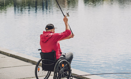 Person with a physical disability who uses wheelchair fishing from fishing pier.の写真素材