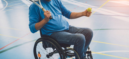 Adult man with a physical disability who uses wheelchair playing tennis on indoor tennis court