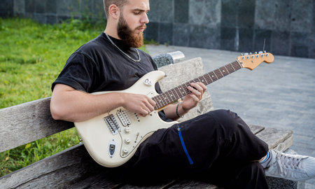 Young street musician playing guitar while sitting on the bench