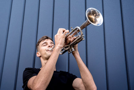 Young street musician playing the trumpet near the big blue wallの写真素材