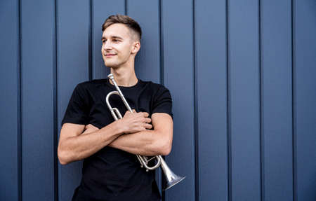 Young street musician playing the trumpet near the big blue wallの写真素材