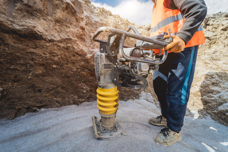 Worker uses a portable vibration rammer at construction of a power transmission substation