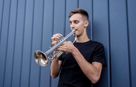 Young street musician playing the trumpet near the big blue wallの写真素材
