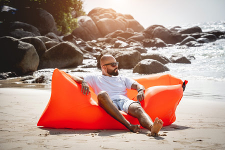 Young man relaxing on the beach while sitting on an inflatable sofa