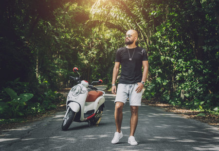 Stylish young man and his motorbike on the road in the jungle