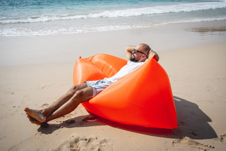 Young man relaxing on the beach while sitting on an inflatable sofaの写真素材