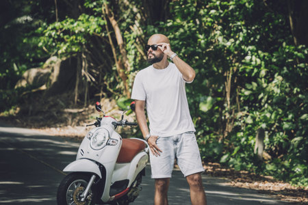 Stylish young man and his motorbike on the road in the jungle