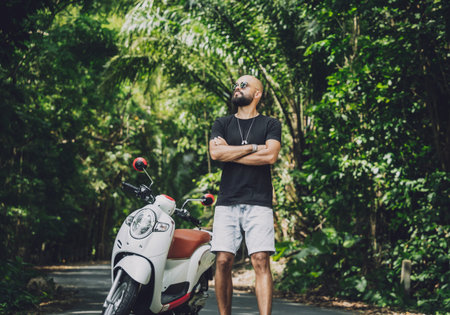 Stylish young man and his motorbike on the road in the jungle