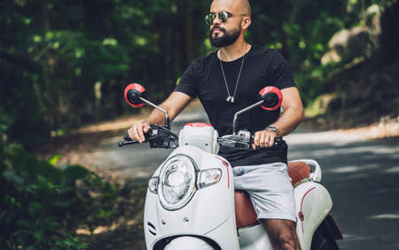 Stylish young man and his motorbike on the road in the jungleの写真素材