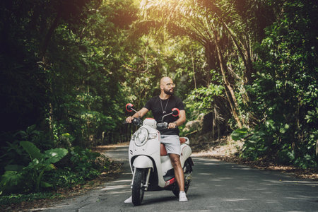 Stylish young man and his motorbike on the road in the jungle