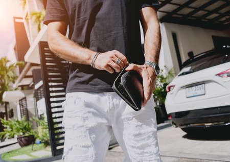 Young businessman holding wallet in his hands against his modern home with garage and carの写真素材