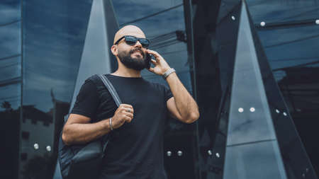 Portrait of a fashion young man talking by the phone at beautiful dark urban backgroundの写真素材