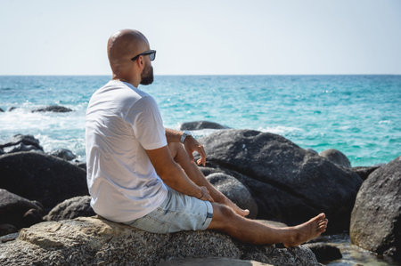 Young man relaxing on the beach while sitting on an stones