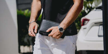 Young businessman holding wallet in his hands against his modern home with garage and carの写真素材
