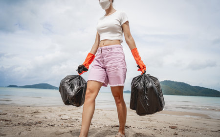 A female ecologist volunteer cleans the beach on the seashore from plastic and other wasteの写真素材
