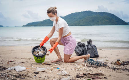 A female ecologist volunteer cleans the beach on the seashore from plastic and other wasteの写真素材