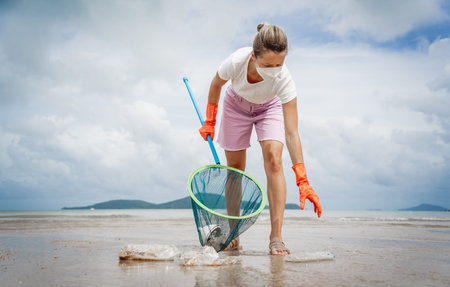 A female ecologist volunteer cleans the beach on the seashore from plastic and other waste