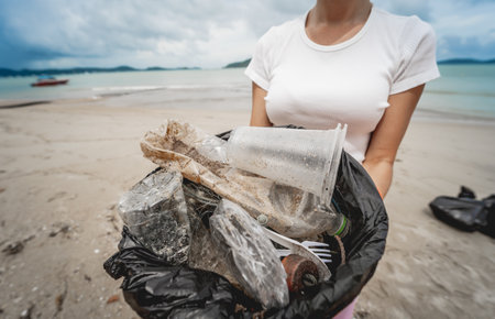 A female ecologist volunteer cleans the beach on the seashore from plastic and other wasteの写真素材