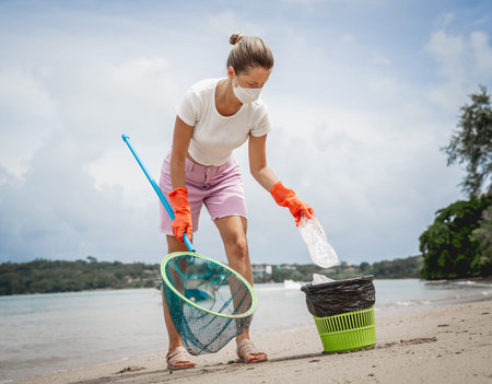 A female ecologist volunteer cleans the beach on the seashore from plastic and other wasteの写真素材