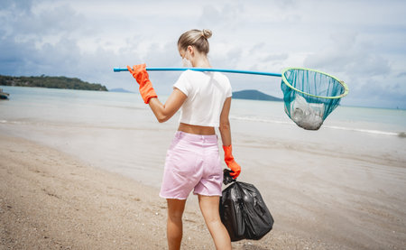 A female ecologist volunteer cleans the beach on the seashore from plastic and other wasteの写真素材