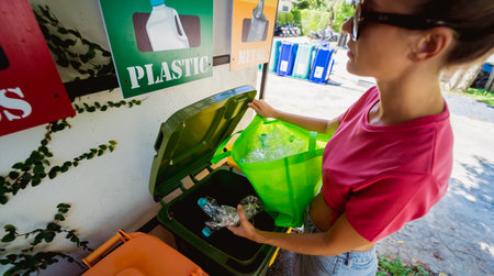 A young beautiful girl throws sorted garbage into special bins