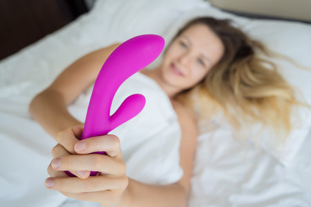 Young sexy woman in the bed holding in her hands a sex toy for adults