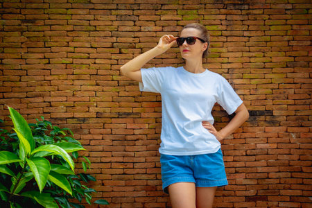 Female model wearing white blank t-shirt on the background of an bricks wall.