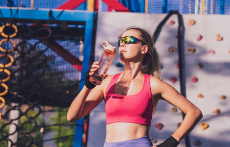 Athletic young woman drinking water after working out and climbing at the artificial rock in training camp.の写真素材