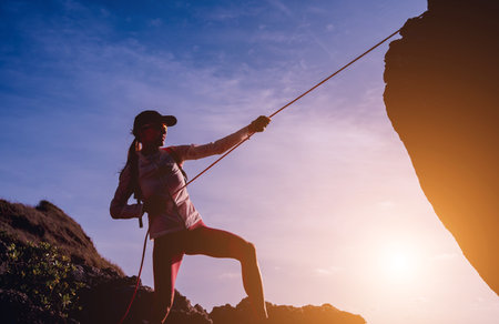 Young woman with a rope climbs to the top in the mountains near the oceanの写真素材