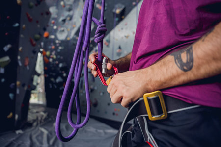 A strong male climber climbs an artificial wall with colorful grips and ropes.