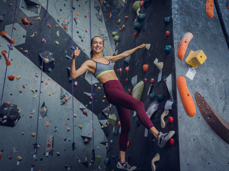 A strong female climber climbs an artificial wall with colorful grips and ropes.の写真素材