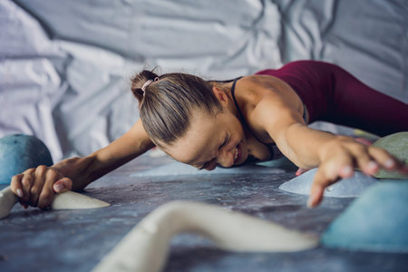 A strong female climber climbs an artificial wall with colorful grips and ropes.の写真素材