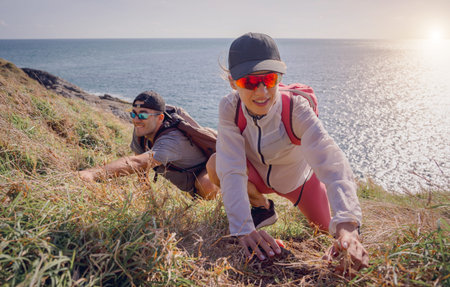 Happy young couple climbs to the top in the mountains near the oceanの写真素材