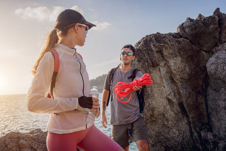 Young couple climbs with a rope to the top in the mountains near the ocean