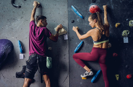 A strong couple of climbers climb an artificial wall with colorful grips and ropes.の写真素材