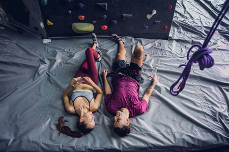A strong couple of climbers relax near artificial wall with colorful grips and ropes.の写真素材