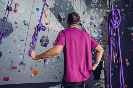 A strong male climber against an artificial wall with colorful grips and ropes.