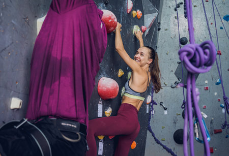 A strong couple of climbers climb an artificial wall with colorful grips and ropes.の写真素材