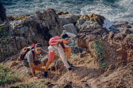 Happy young couple climbs to the top in the mountains near the oceanの写真素材