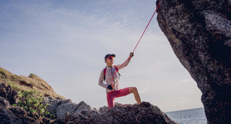 Young woman with a rope climbs to the top in the mountains near the oceanの写真素材