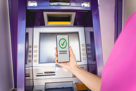 Young woman using the smart phone for cardless withdrawing the cash near the ATMの写真素材