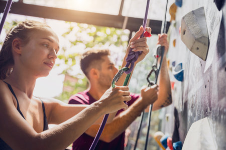 A strong couple of climbers climb an artificial wall with colorful grips and ropes.