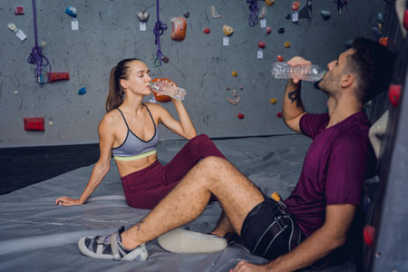 A strong couple of climbers relax near artificial wall with colorful grips and ropes.の写真素材