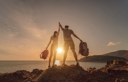 Happy young couple climbs to the top in the mountains near the oceanの写真素材