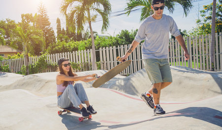 Young happy couple with skateboards enjoy longboarding at the skatepark