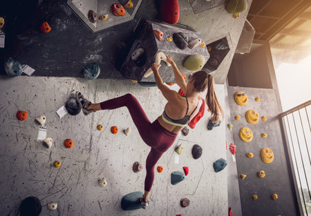 A strong female climber climbs an artificial wall with colorful grips and ropes.の写真素材