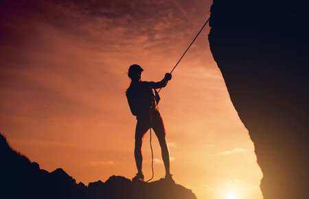 Young woman with a rope climbs to the top in the mountains near the ocean